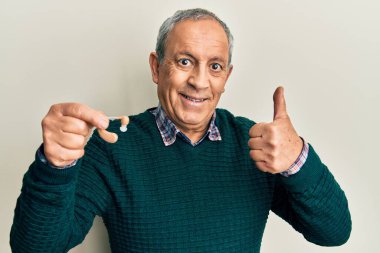 Gri saçlı, elinde tıbbi işitme cihazı olan yakışıklı, mutlu ve olumlu gülümseyen, başparmağını kaldıran, mükemmel ve onay işareti olan yaşlı bir adam. 