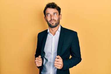 Sakallı, takım elbiseli, ceketli, gülümseyen, yan bakan ve düşünen yakışıklı bir adam.. 