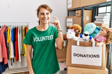 Bağışta gönüllü tişört giyen güzel beyaz kadın gülümsüyor ve el hareketleriyle küçük beden işareti yaparak kameraya bakıyor. ölçüm kavramı. 