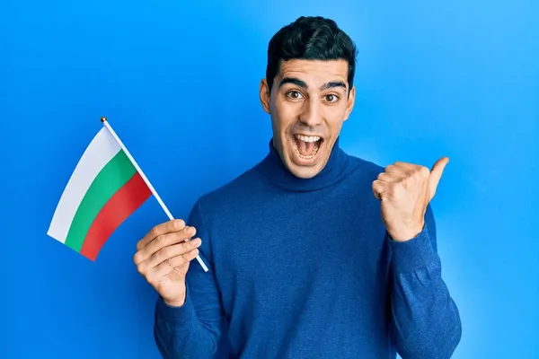 Hombre Hispano Guapo Sosteniendo Bandera Bulgara Señalando Pulgar Hacia Lado —  Fotos de Stock