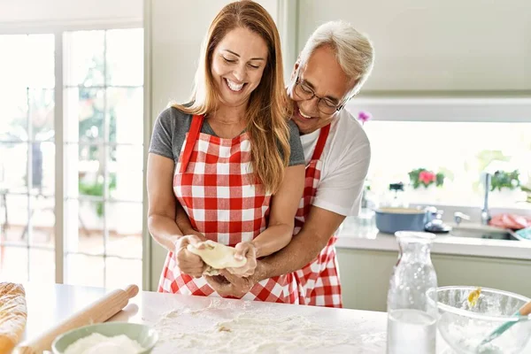Orta yaşlı İspanyol çift mutlu gülümsüyor ve mutfakta ekmek pişiriyor..