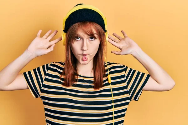 Redhead Young Woman Listening Music Using Headphones Making Fish Face — Stockfoto
