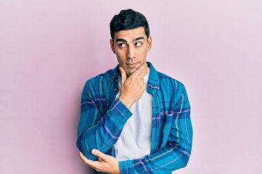 Elleri çenesinde gündelik kıyafetler giyen yakışıklı İspanyol bir adam soru soruyor, düşünceli bir yüz ifadesi var. Düşünceli bir yüzle gülümsüyor. şüphe kavramı. 