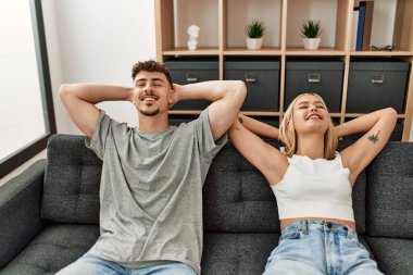 Kafkasyalı genç çift ellerini başının üstüne koyup evdeki kanepede oturuyorlar..