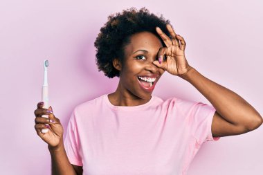Genç Afro-Amerikalı kadın elinde elektrikli diş fırçası, gülümsüyor. Mutluluktan gülümsüyor. 