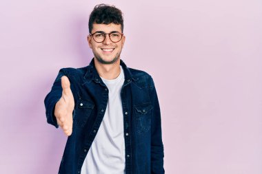 Gündelik kıyafetler ve gözlük takan genç İspanyol adam dostça bir selamlama ve hoş geldin hediyesi olarak el sıkışmayı sunuyor. başarılı iş. 