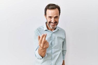 Orta yaşlı, sakallı, soyutlanmış arka planda dikilen İspanyol bir adam, el hareketleriyle, mutlu bir şekilde karşılamaya ve gülümsemeye davet ediyor. 