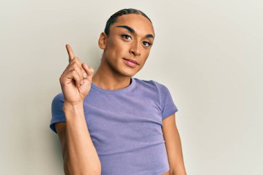 Makyaj yapan, uzun saçlı, günlük tişörtlü İspanyol bir numarayı gösterip işaret ederken kendinden emin ve mutlu bir şekilde gülümsüyor.. 