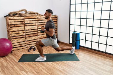 Genç Arap adam gülümsüyor spor merkezinde kettlebell ile antrenman yapıyor.