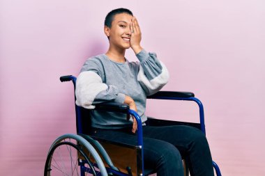 Kısa saçlı güzel İspanyol kadın tekerlekli sandalyede oturuyor. Bir gözünü eliyle kapatıyor. Yüzünde kendine güvenen bir gülümseme ve sürpriz bir duygu var.. 