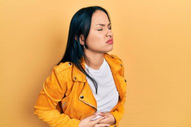 Burnunda piercing olan güzel bir İspanyol kadın elleri karnında sarı deri ceket giyiyor çünkü hazımsızlık, acı verici bir hastalık kendini iyi hissetmiyor. Ağrı kavramı. 