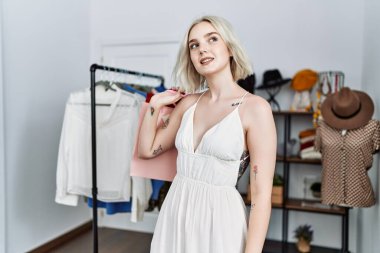 Giysi dükkanında kendine güvenen, gülümseyen beyaz bir kadın.