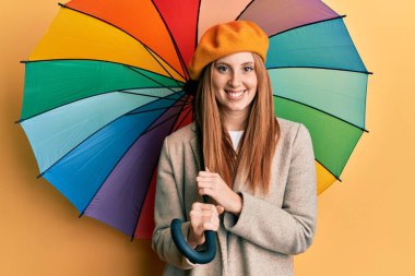 Fransız tarzı giyinen genç İrlandalı kadın elinde renkli bir şemsiye tutarken pozitif ve mutlu görünüyor ve gülümsüyor. 