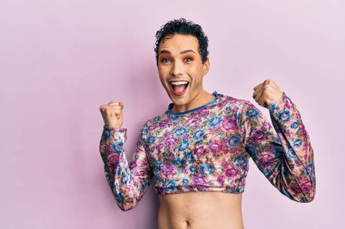 Makyaj elbisesi giymiş yakışıklı bir adam. Şaşırmış ve şaşırmış bir şekilde kolları açık ve gözleri açık bir şekilde başarıyı kutluyor. Kazanan konsept. 