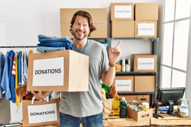 Gönüllü olarak bağış kutusunu tutan yakışıklı orta yaşlı bir adam yüzünde kocaman bir gülümsemeyle kameraya el ile işaret ediyor.. 