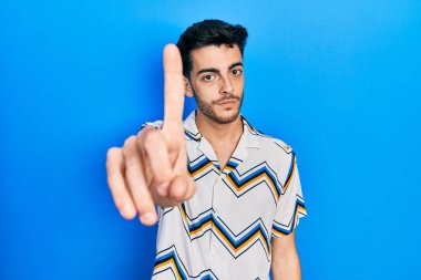 Latin asıllı genç bir adam, gündelik giysiler giyip parmağını kaldırmış ve kızgın bir ifade takınıyor. 