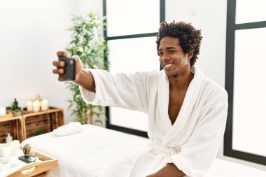 Genç Afrikalı Amerikalı gülümseyen adam güzellik merkezindeki akıllı telefondan özçekim yapıyor.