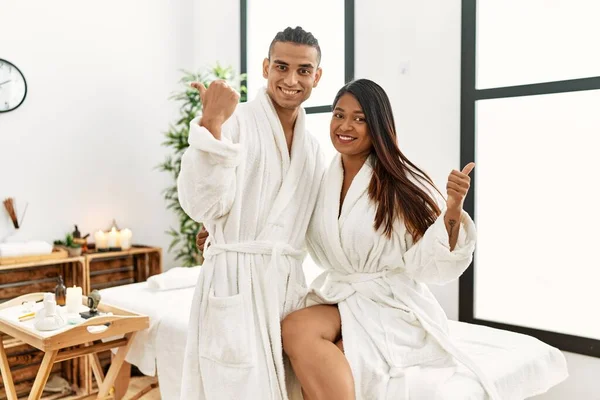 Young Latin Couple Wearing Towel Standing Beauty Center Pointing Back — Stockfoto