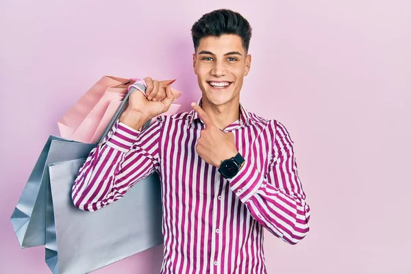 Jovem Hispânico Segurando Sacos Compras Sorrindo Feliz Apontando Com Mão — Fotografia de Stock