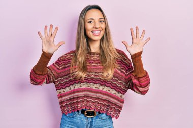 Güzel İspanyol kadın hippi süveteri giyer ve parmaklarıyla on numarayı gösterirken kendine güvenen ve mutlu bir şekilde gülümser.. 