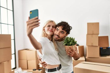 Genç ve güzel bir çift mutlu bir şekilde gülümsüyor. Yeni evlerinde akıllı telefonların yanında selfie çekiyorlar..