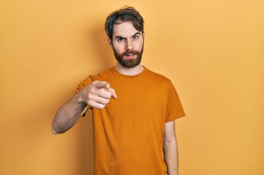 Sakallı, sarı tişörtlü beyaz bir adam kameraya kızgın ve sinirli olduğunu gösteriyor. 