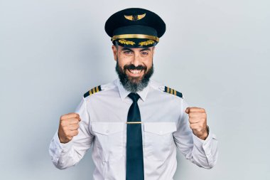 Young hispanic man wearing airplane pilot uniform celebrating surprised and amazed for success with arms raised and open eyes. winner concept. 