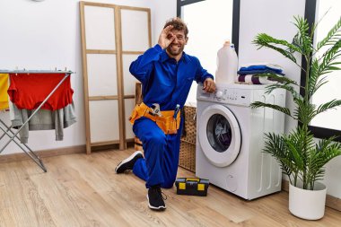 Çamaşır makinesinde çalışan Latin asıllı genç adam gülümsüyor. Mutluluktan gülümsüyor. 