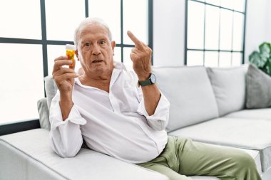 Senior man holding pills showing middle finger, impolite and rude fuck off expression 