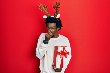 Geyik Noel şapkası takan genç Afro-Amerikalı bir adam elinde hediyeyle pis ve iğrenç bir koku, katlanılmaz bir koku, nefesini burnunda tutarak nefes alıyor. Kötü kokuyor. 