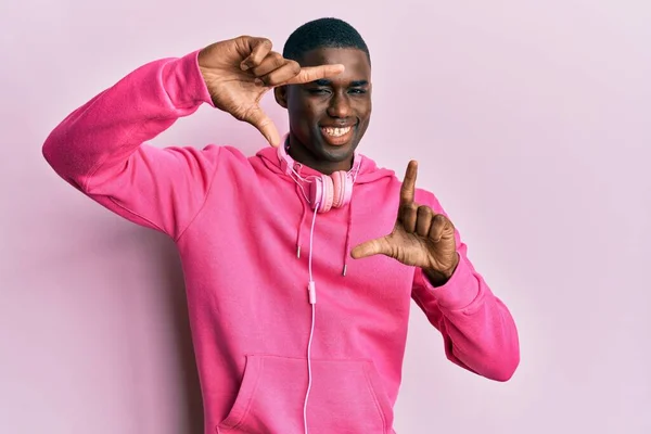 若いアフリカ系アメリカ人の男性は ジムの服を着て 幸せな顔をした手と指でフレームを作るヘッドフォンを使用しています 創造性と写真の概念 — ストック写真