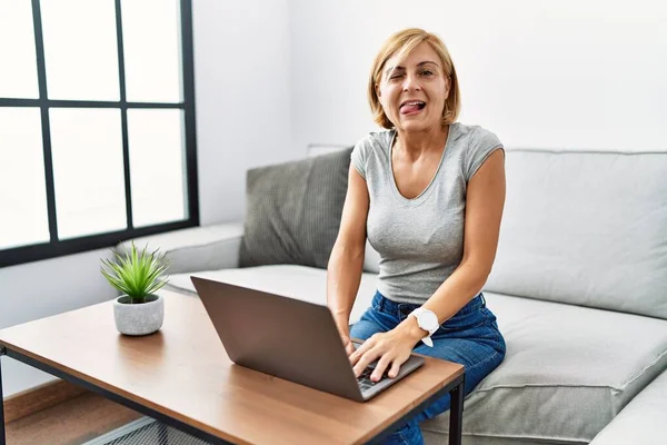 Medelålders Blond Kvinna Använder Laptop Hemma Sticker Tungan Glad Med — Stockfoto
