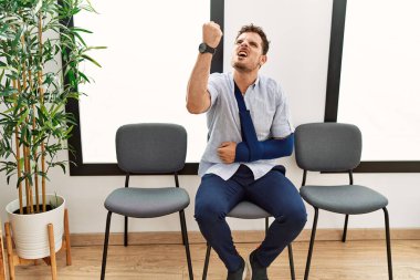 Yakışıklı genç adam, kolundan sakatlanmış, kızgın ve kızgın bir şekilde bekleme odasında oturmuş öfkeyle bağırırken yumruğunu kaldırıyor. öfke ve agresif konsept. 