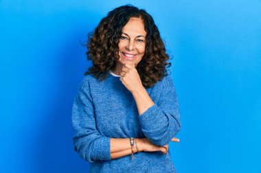 Orta yaşlı İspanyol kadın gündelik kıyafetler giyiyor kameraya bakıyor kollarını kavuşturup gülümsüyor ve çenesini kaldırıyor. Olumlu düşünmek. 