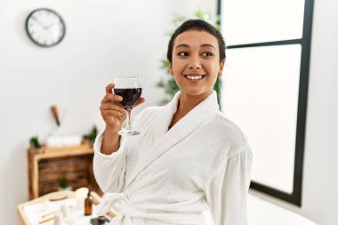 Genç İspanyol kadın bornoz giyip güzellik merkezinde şarap içiyor.