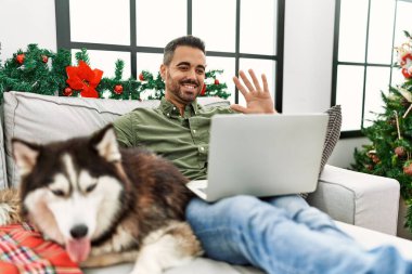 Genç İspanyol adamın evdeki Noel ağacının yanında köpekle kanepede otururken görüntülü konuşması var.