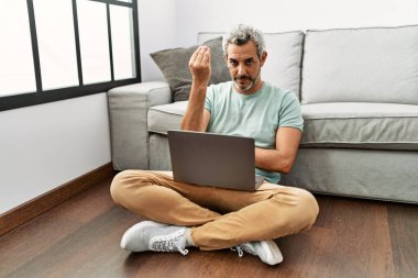 Orta yaşlı İspanyol bir adam oturma odasında dizüstü bilgisayar kullanıyor. İtalyan jestleri yapıyor. Elleri ve parmakları kendinden emin bir ifadeyle. 