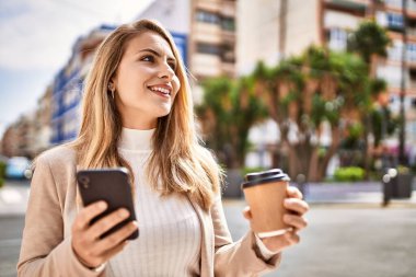 Sokakta akıllı telefon kullanan, kendine güvenen genç sarışın kadın.
