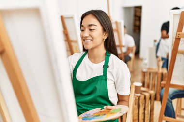 Sanat stüdyosundaki bir grup insanla mutlu bir resim çizen genç bir kadın..