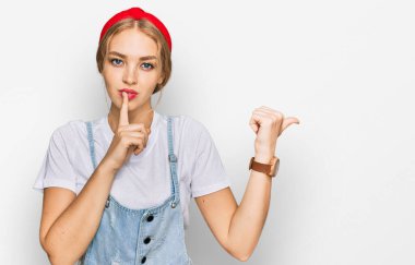 Gündelik giysiler giymiş genç beyaz bir kız sessiz olmak istiyor. Parmakları dudaklarında, elleri yandan işaret ediyor. sessizlik ve gizli konsept. 