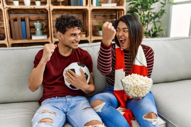 Evdeki kanepede oturan genç latin çift futbol maçını izliyor ve destekliyor..