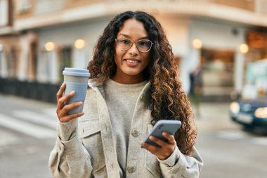 Genç Latin kadın akıllı telefon kullanıyor ve şehirde kahve içiyor..