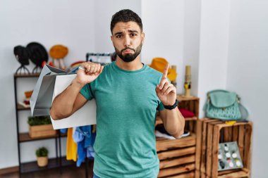 Satış mağazasında sakallı, alışveriş torbaları tutan, üzgün ve üzgün görünen, yönünü parmaklarıyla gösteren, mutsuz ve depresif bir genç adam.. 