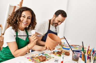 Sanat okulunda kilden heykel çizerken gülümseyen iki orta yaşlı öğrenci..