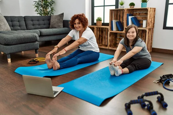 Mature mother and down syndrome daughter doing exercise at home. Stretching at the living room