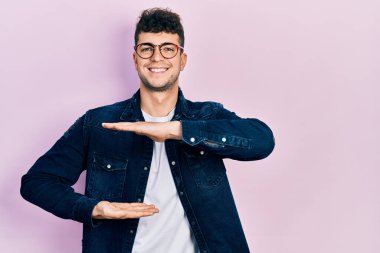 Gündelik kıyafetler giyen ve büyük boy ve ölçü işareti gösteren el kol hareketleri yapan Latin kökenli genç bir adam. Kameraya bakıp gülümsüyor. ölçüm kavramı. 