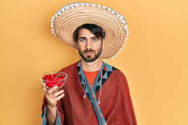 Meksika şapkası takan genç İspanyol bir adam. Elinde kırmızı biber, düşünceli ve ayık bir ifade var. Kendine güveniyor gibi görünüyor. 