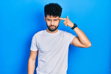 Beyaz tişörtlü sakallı genç Arap adam alnında sivilce çıkmasından mutsuz, siyah noktalı çirkin bir enfeksiyon taşıyor. sivilce ve deri problemi 