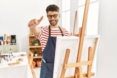 Sanat stüdyosundaki Arap genç adam elleriyle olumlu jest yapmayı onaylıyor, gülümsüyor ve başarı için seviniyor. kazanan jest. 