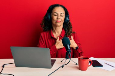 Güzel orta yaşlı bir kadın radyo stüdyosunda çalışıyor. Elleri göğsünde, gözleri kapalı ve yüzünde minnet dolu bir jest ile gülümsüyor. sağlık kavramı. 